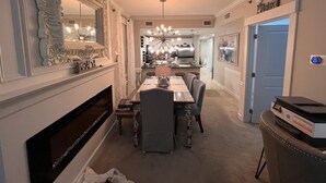 A dining area with a fireplace, a chandelier, and a kitchen in the background.