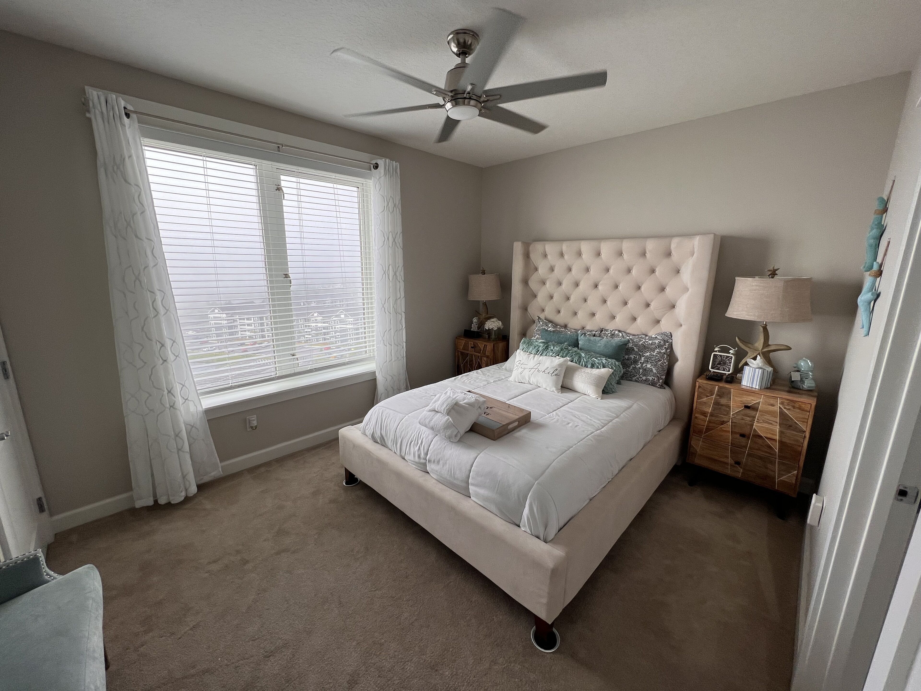 A bedroom with a bed, a ceiling fan, a nightstand, and a window with blinds.