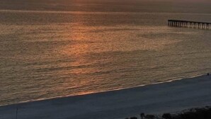 A sunset over a calm sea with a pier extending into the water.