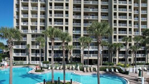 A multi-story hotel with a swimming pool surrounded by palm trees.