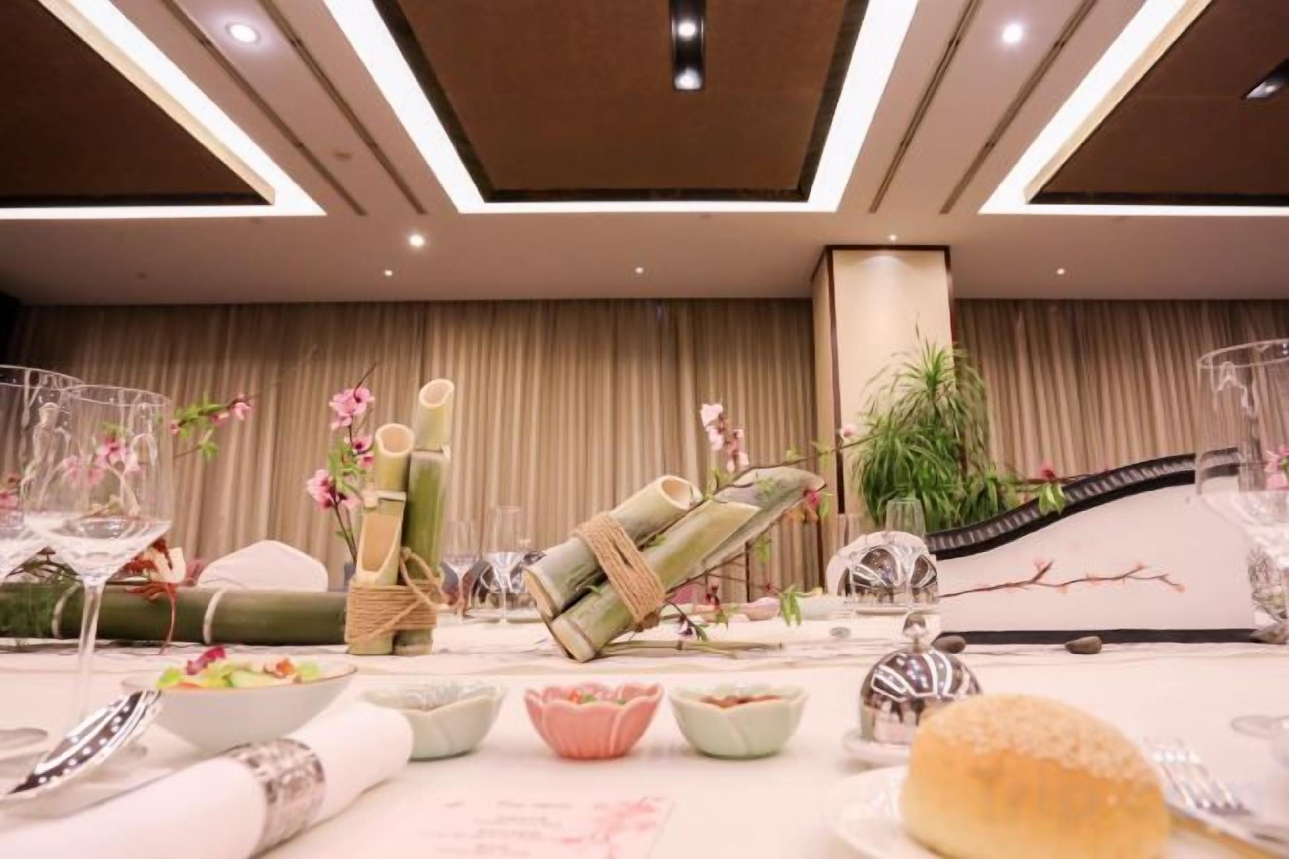 A table set with glassware, plates, and a bread roll, with a plant and decorative items in the background.