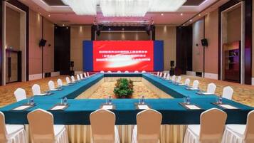 A conference room with a long table, white chairs, and a large screen at the front.