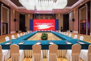 Un salón de conferencias con una mesa larga, sillas blancas y una pantalla grande al frente.