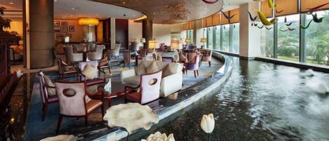 A spacious lobby with a curved ceiling, seating areas, and a water feature.