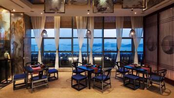 A hotel room with a large window, multiple tables and chairs, and a view of the cityscape.