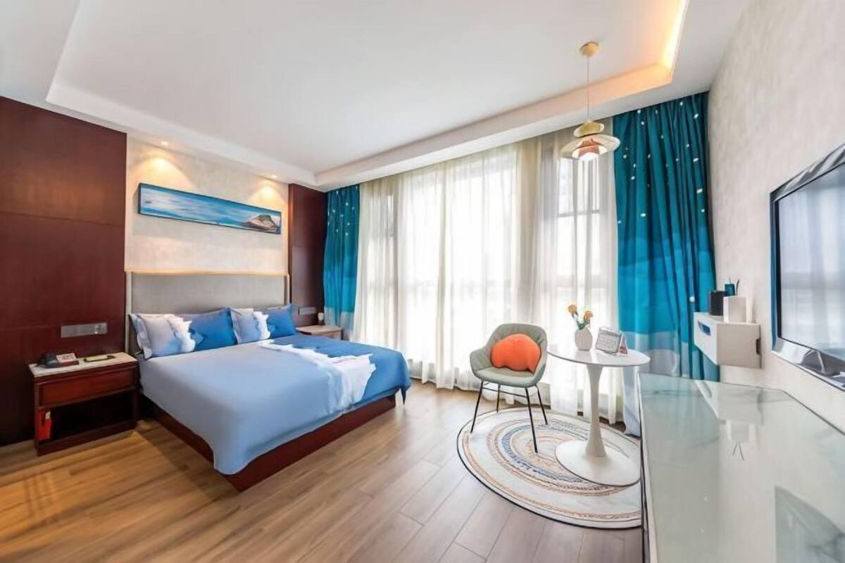 Habitación de hotel con una cama grande, un escritorio con silla, televisión y ventana con cortinas.