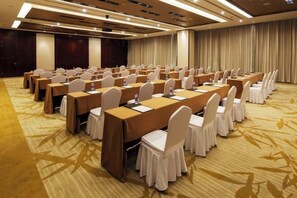 Un salón de conferencias con mesas y sillas dispuestas en filas, suelo alfombrado y un telón de fondo.