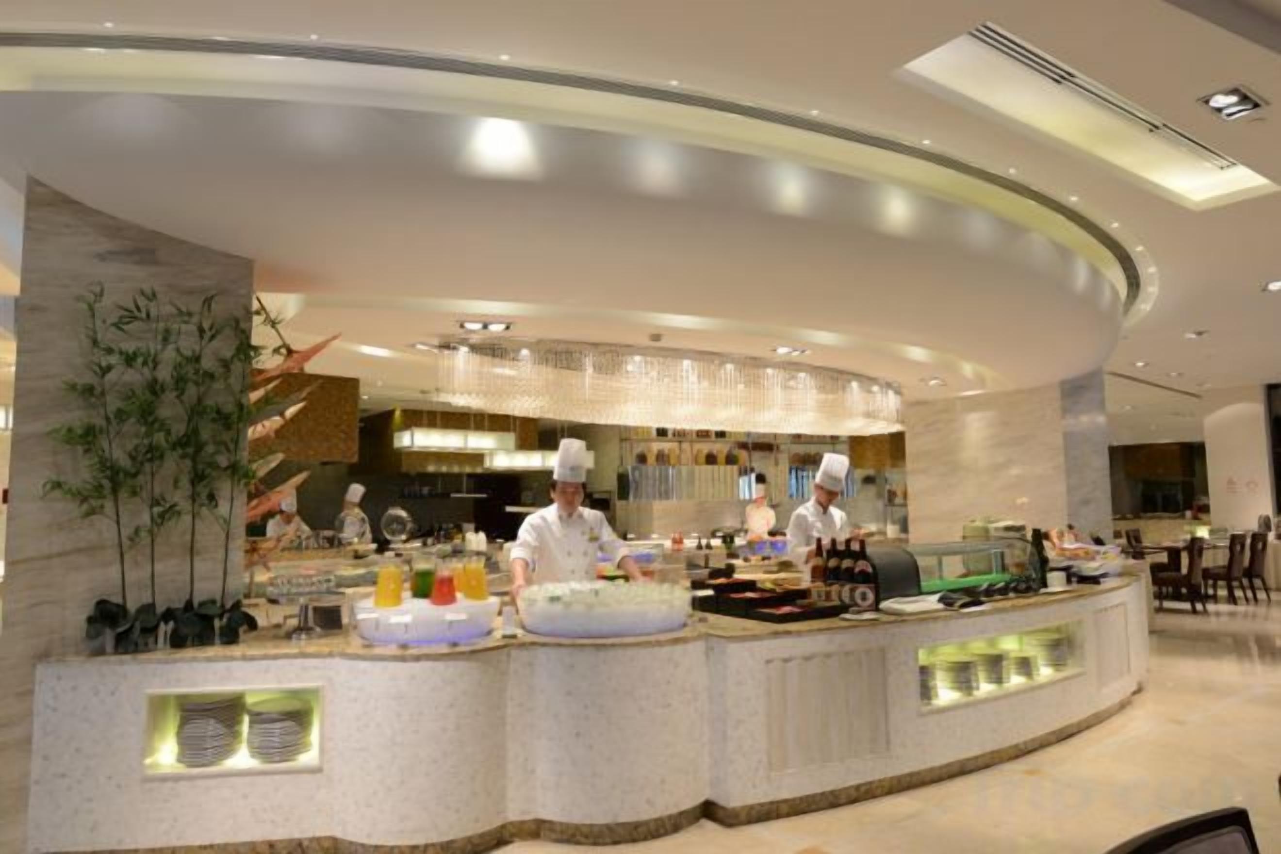 A modern kitchen with chefs preparing food, a curved counter, and a well-lit interior.