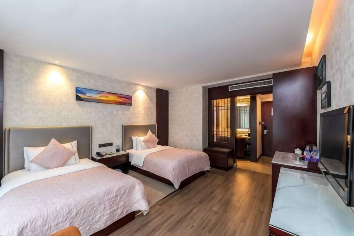 Habitación de hotel con dos camas, un escritorio, un televisor y un cuadro en la pared.