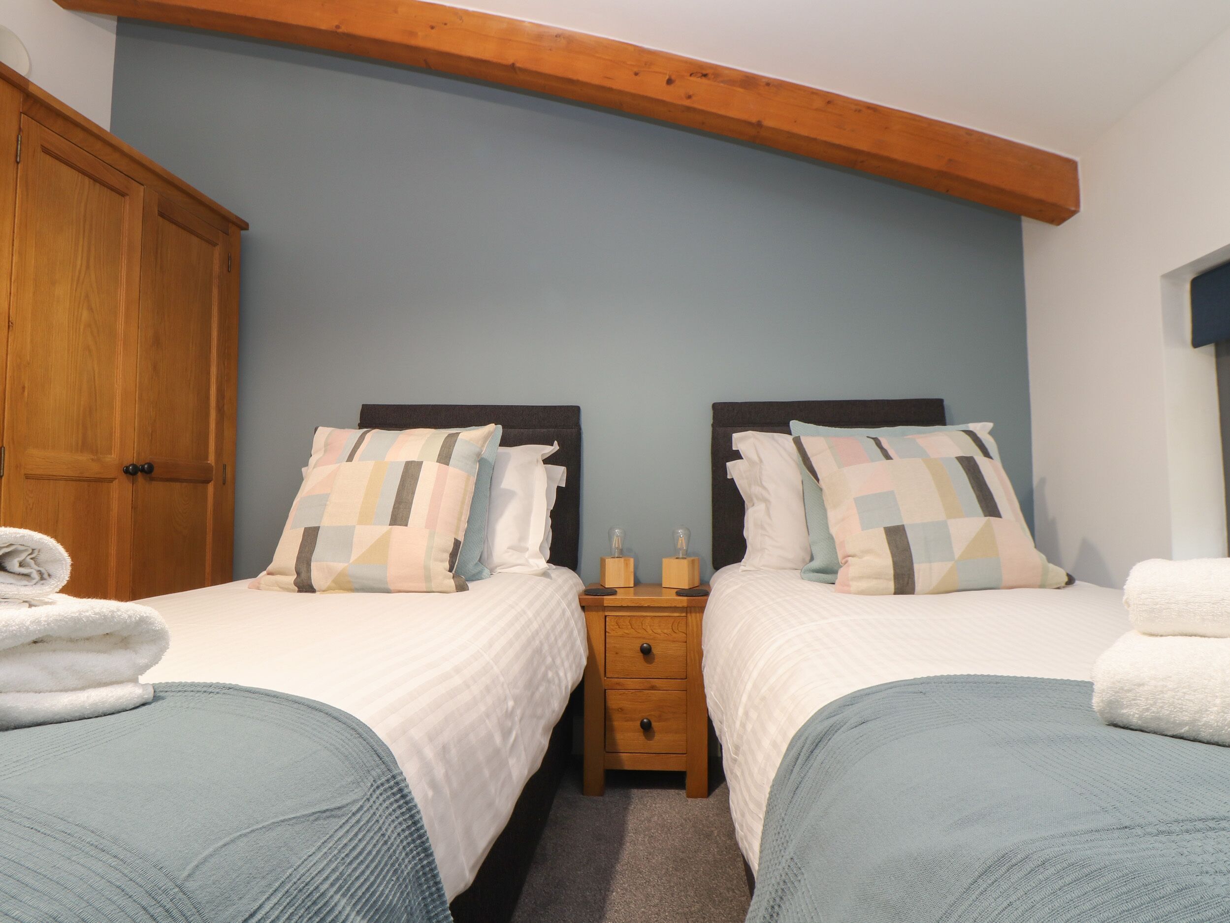 A bedroom with two beds, wooden wardrobe, and a nightstand with a lamp.