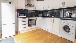 Une cuisine moderne avec des meubles blancs, un four à micro-ondes, un four, un grille-pain et un lave-linge.