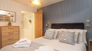 Une chambre à coucher comprenant un lit, une commode en bois, un miroir, un luminaire suspendu et une porte donnant sur une salle de bain.