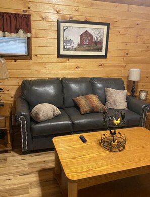 Ein gemütliches Zimmer mit einem Ledersofa, einem Holztisch und einem Bilderrahmen mit einem Bild einer Scheune an der Wand.