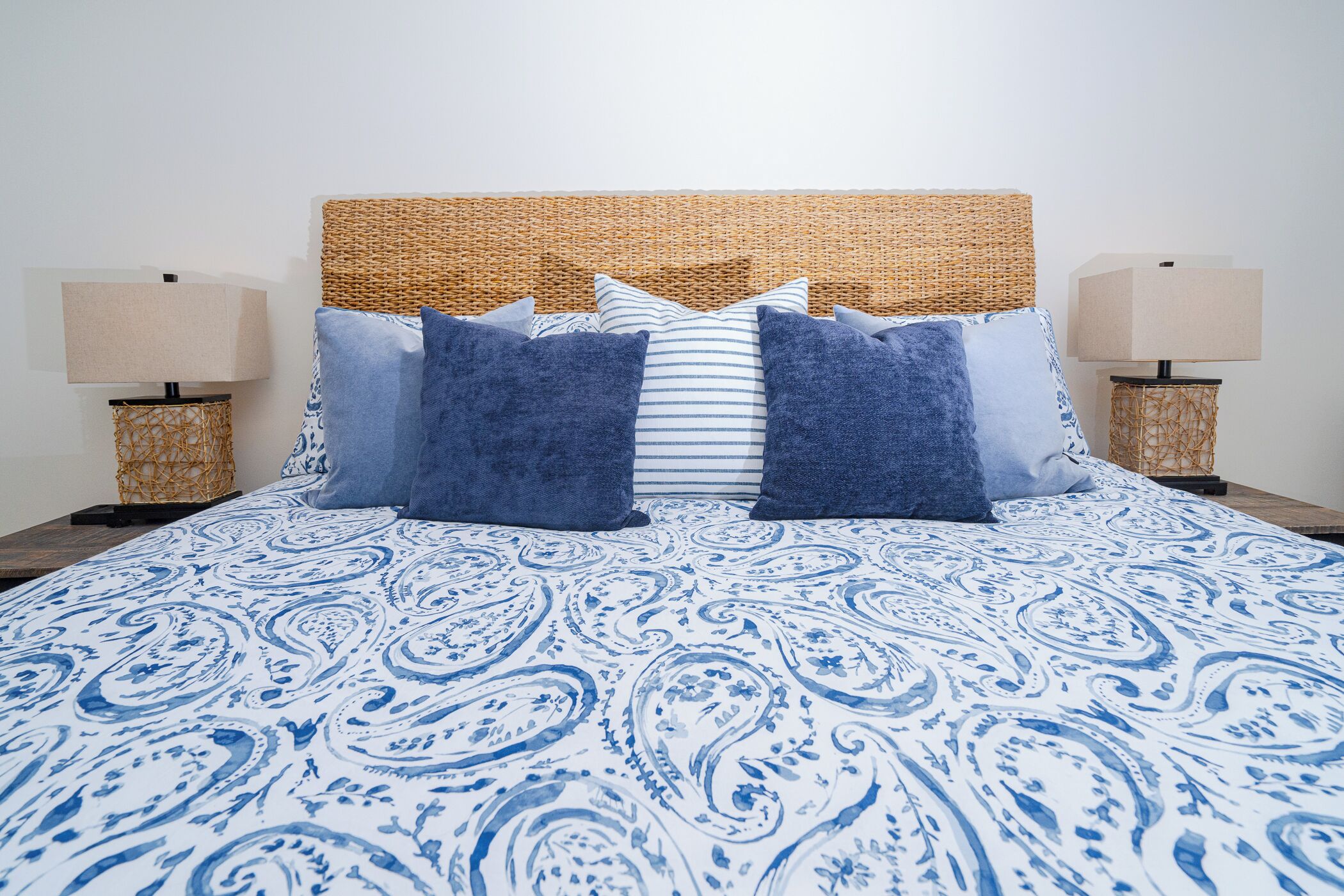 A bed with a blue and white patterned bedspread, a woven headboard, and two bedside lamps on wicker stands.