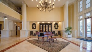 A grand lobby with a piano, large chandeliers, and a high ceiling.