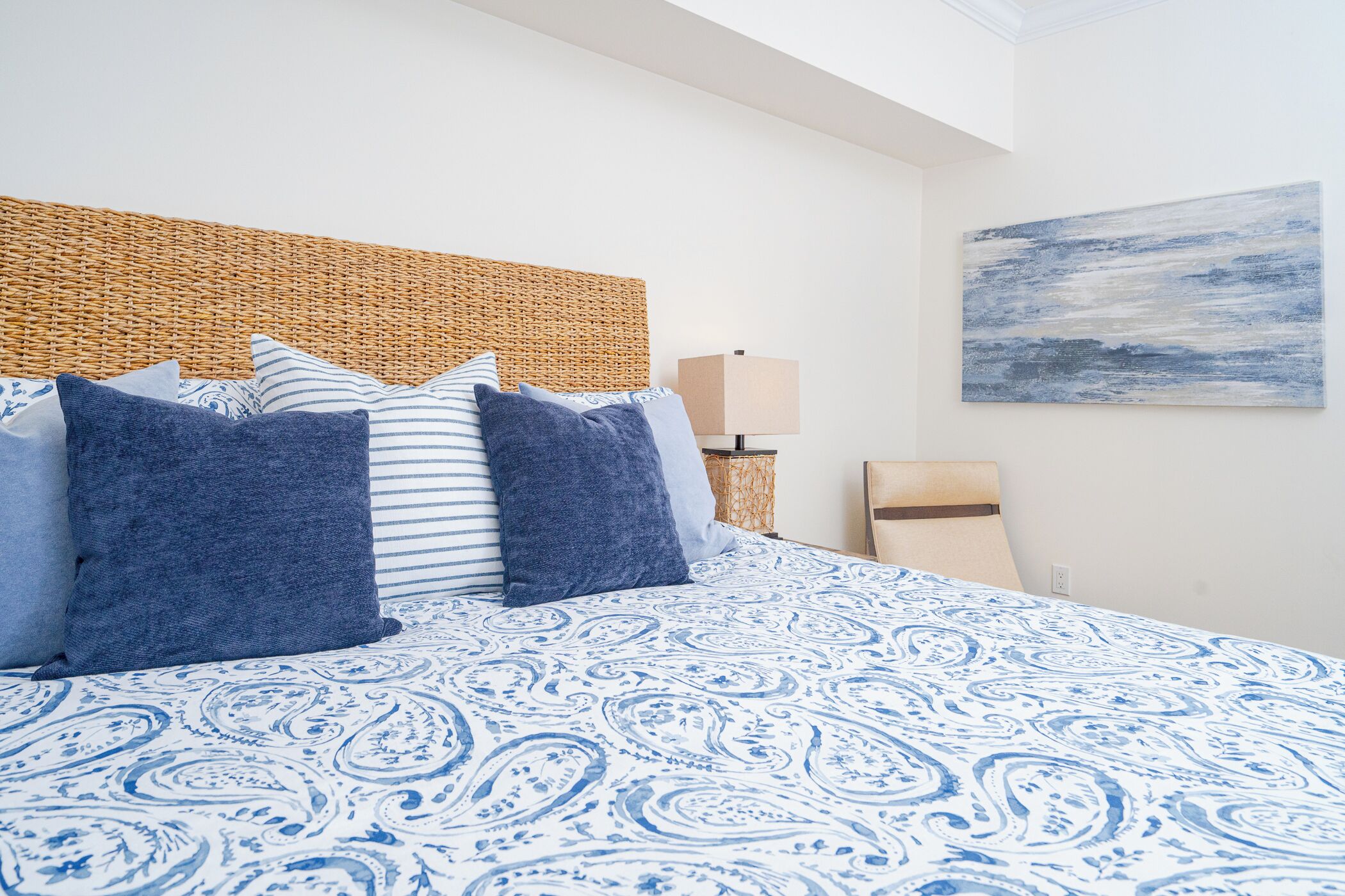 A bedroom with a patterned bedspread, a wicker headboard, and a wall-mounted lamp.