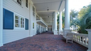 A covered walkway with brick flooring, white columns, and blue shutters.