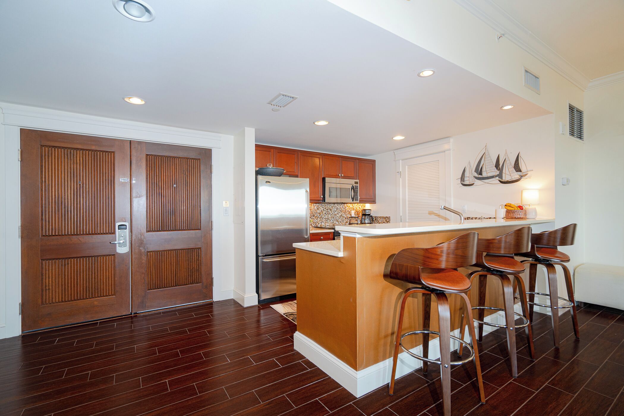 A modern kitchen with wooden cabinets, a stainless steel refrigerator, and a central island with bar stools.