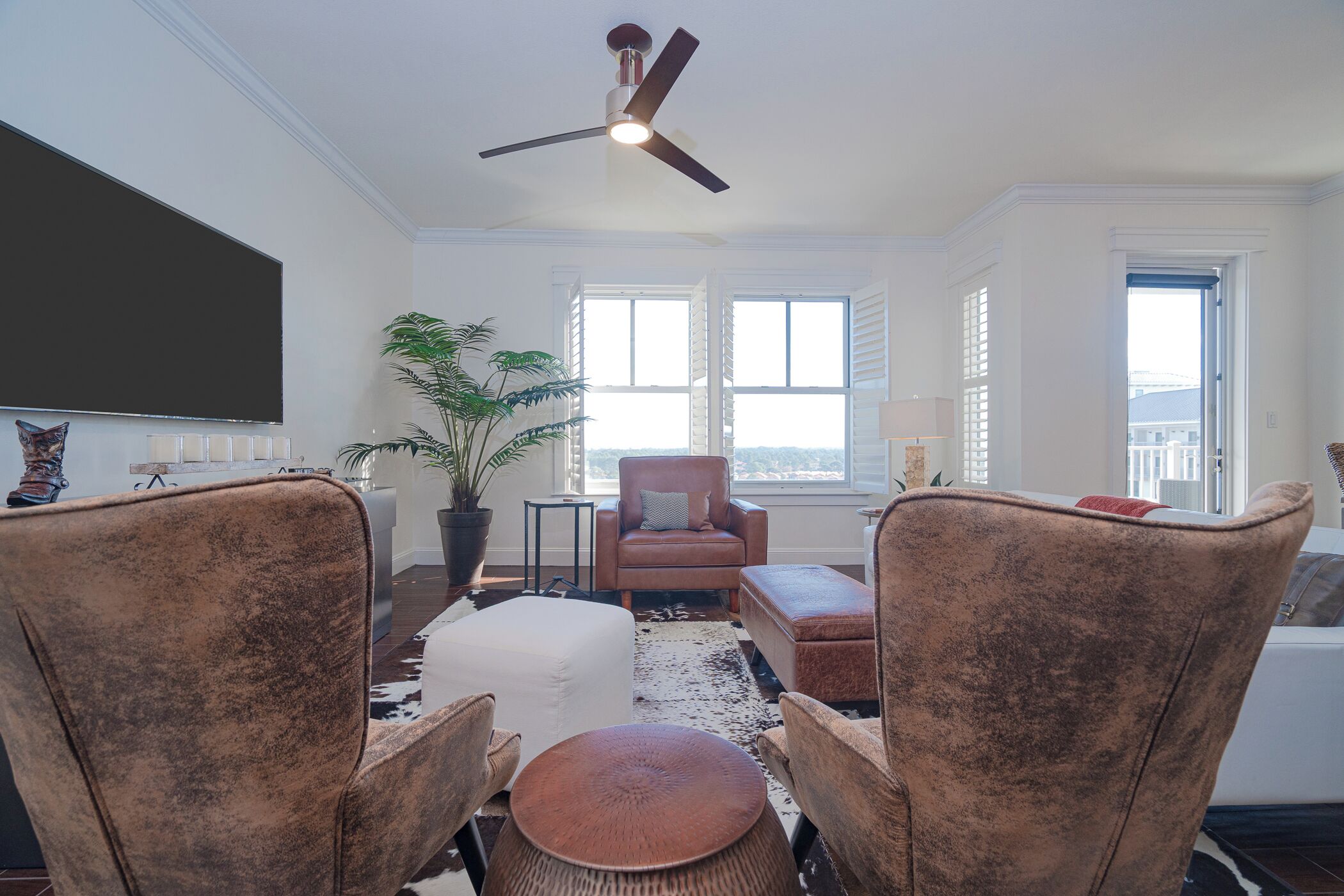 A living room with a ceiling fan, a large window, a potted plant, and a brown leather sofa.