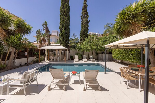 Un espace piscine aménagé avec des chaises longues, une table et une pergola.