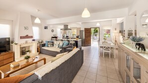 Ein modernes Wohnzimmer mit einer Couch, einem Couchtisch und einem Fernseher. Es gibt eine Küchenzeile mit einem Esstisch und Stühlen.