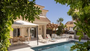 A pool area with lounge chairs, a dining table, and a covered patio. - Protaras Villa Athamas Blue (Protaras)