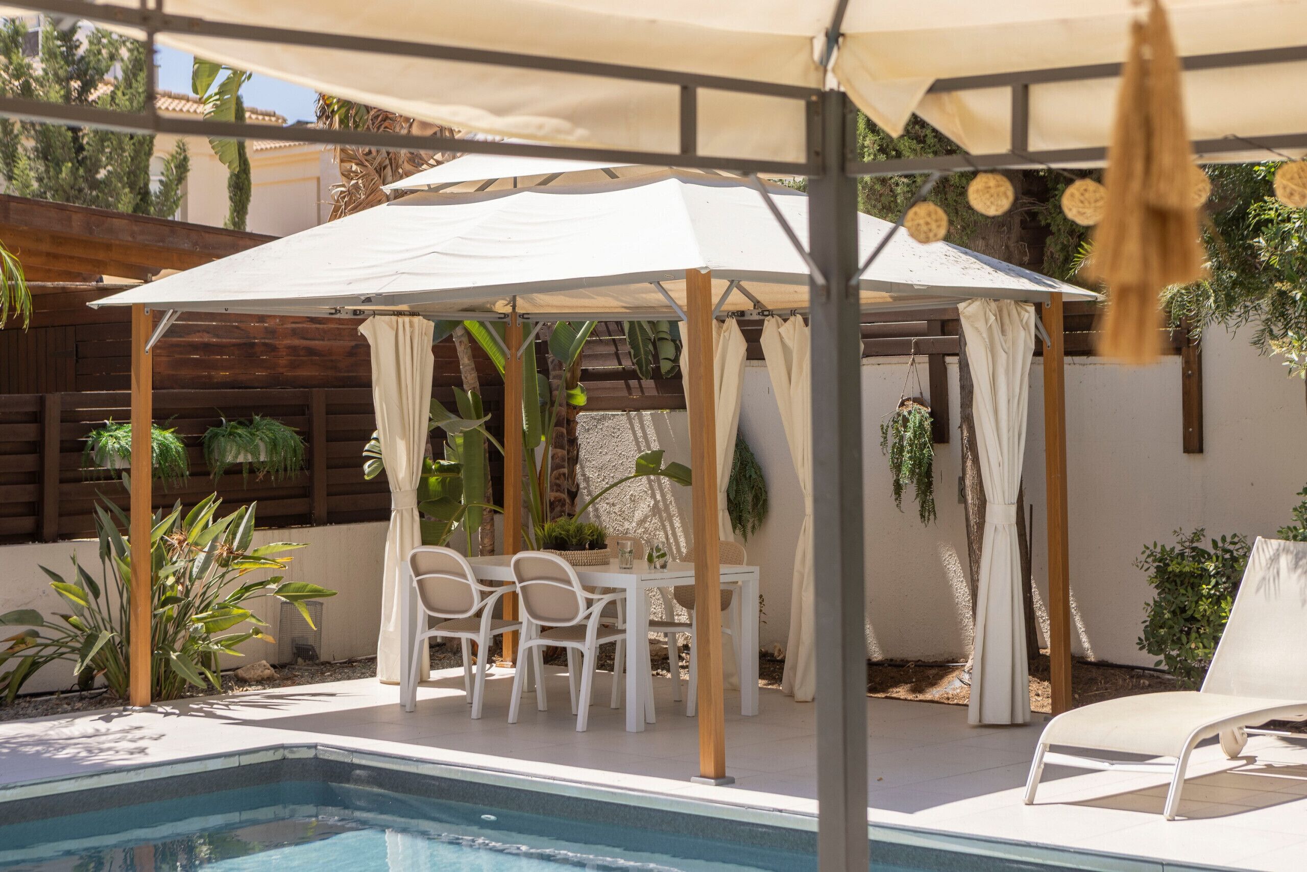A poolside area with a covered seating area, chairs, and a table.