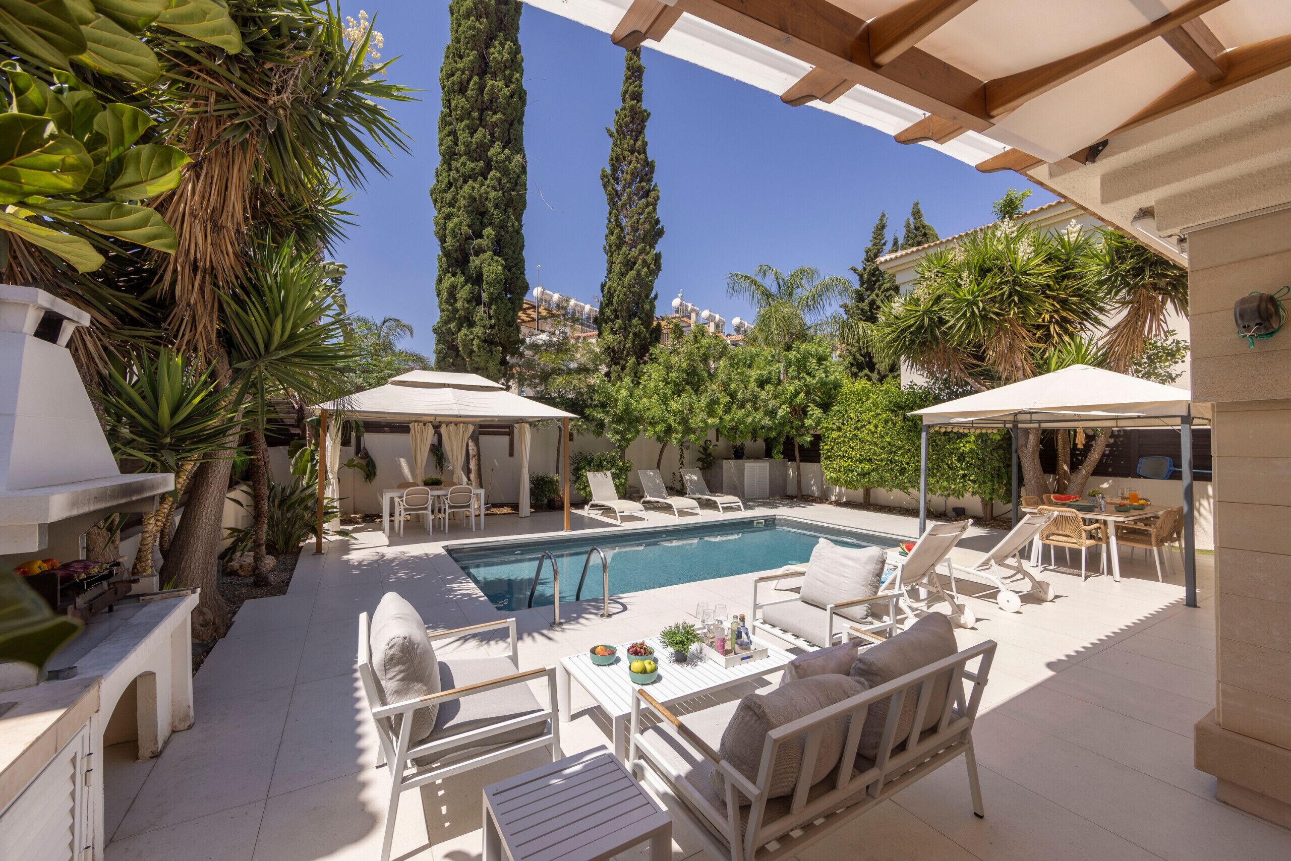 Un espace aménagé au bord de la piscine, avec des chaises longues, un barbecue et une pergola offrant de l’ombre.