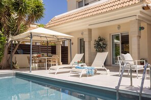 Une piscine avec des chaises longues et un espace salon abrité.