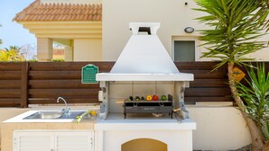 Eine Außenküche mit Spüle, Grill und einem Schild, das Grillregeln aufzeigt.