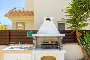 An outdoor kitchen with a sink, a grill, and a sign indicating grilling rules.