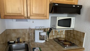 Een kleine keuken met houten kastjes, een magnetron, koffiezetapparaat, spoelbak en vaatwasser.