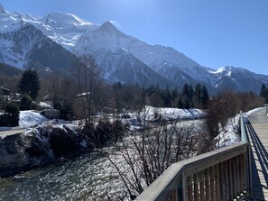 Un pont en bois enjambant une rivière, avec des montagnes enneigées en arrière-plan.