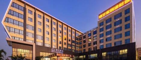 A modern hotel with multiple floors, a parking lot, and a prominent entrance.