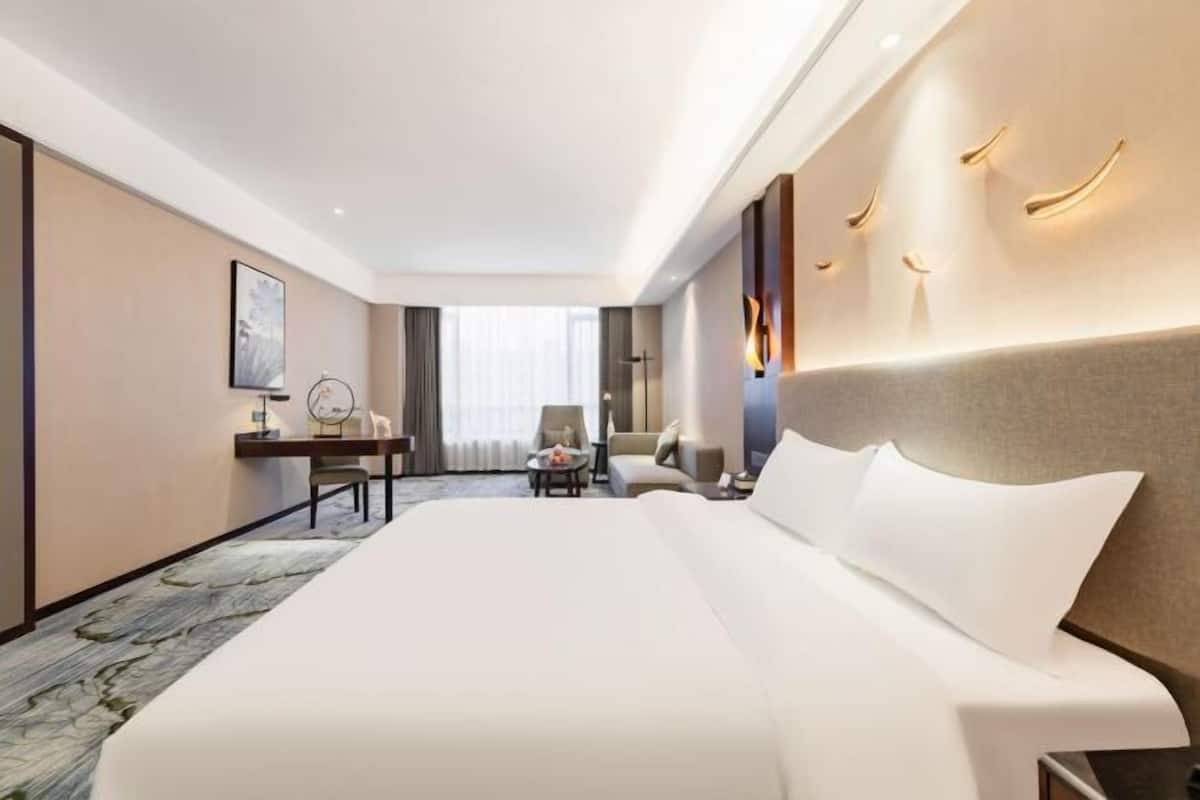 Une chambre d’hôtel avec un grand lit, un bureau avec une chaise, un canapé et une vue sur l’extérieur.