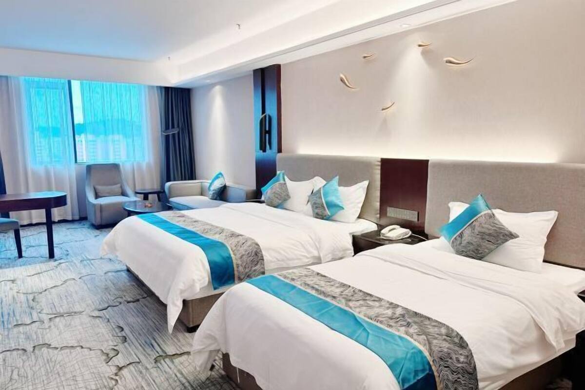 Une chambre d’hôtel avec deux lits, un bureau, une chaise et une grande fenêtre avec des rideaux.