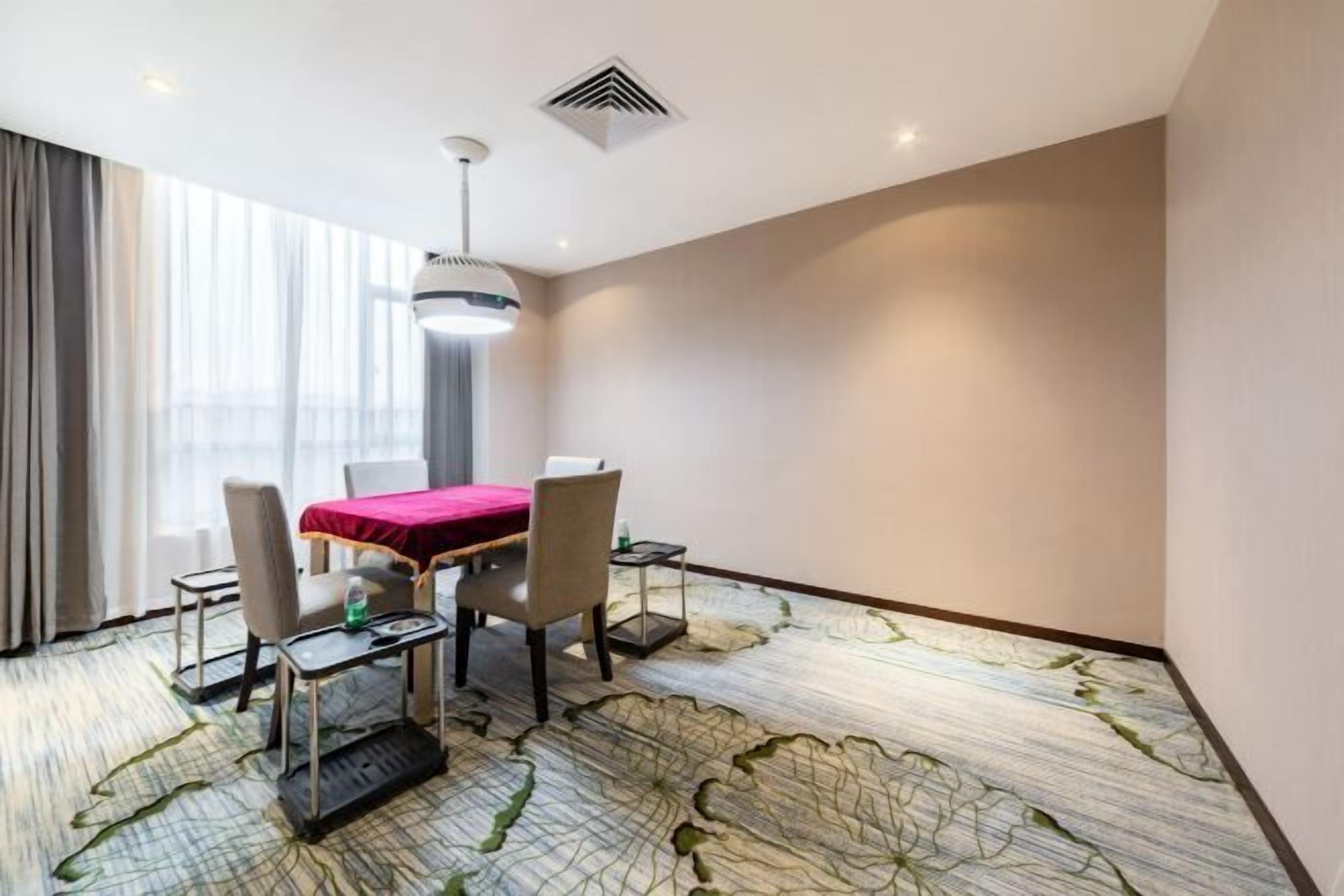 A hotel room with a dining table, chairs, a red tablecloth, a ceiling light, and a patterned carpet.