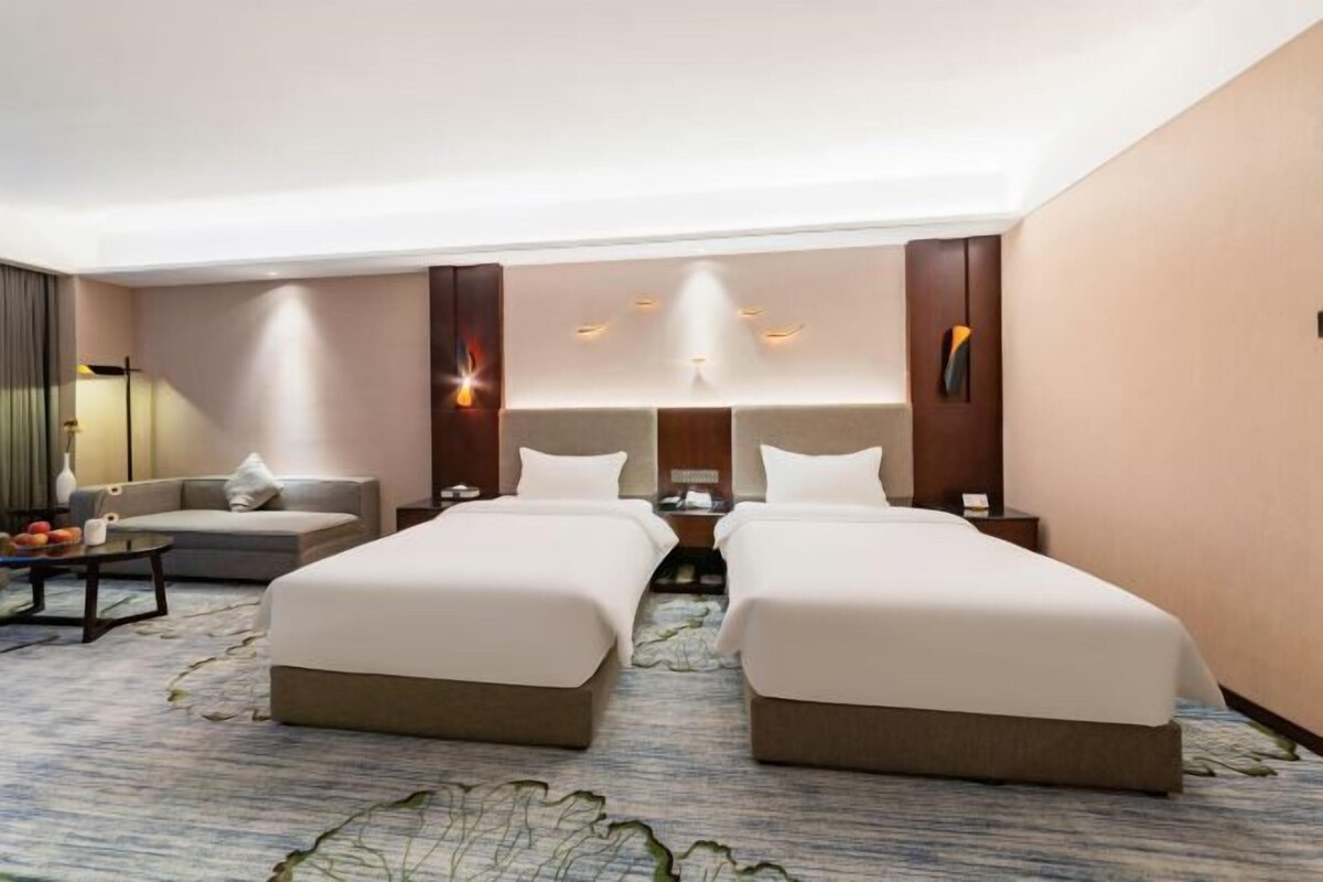 A hotel room with two beds, a sofa, a desk, and a lamp.