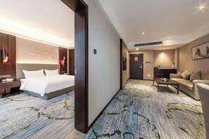 A hotel room with a large bed, a desk, a sofa, and a carpet with a leaf pattern. - Boyi Hotel (Foshan)