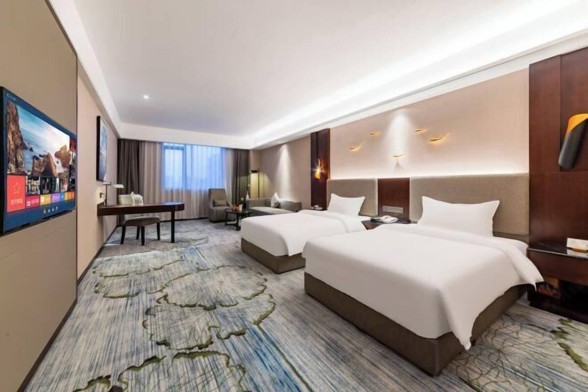 Une chambre d’hôtel avec deux lits, un bureau, une chaise, une télévision et une grande fenêtre.