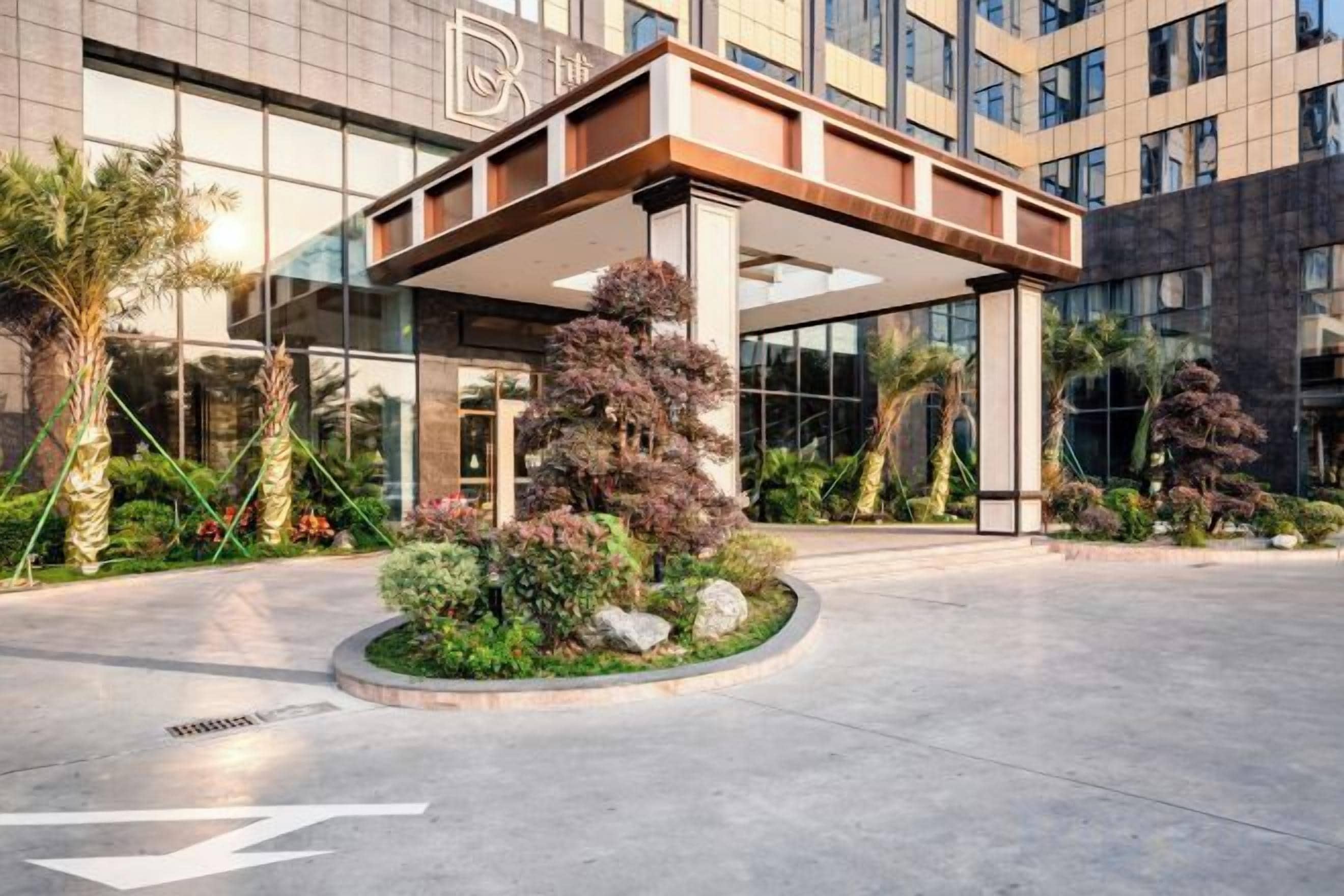 A hotel entrance with a covered walkway, palm trees, and a landscaped area.
