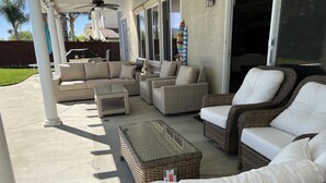 Un patio cubierto con muebles de mimbre, incluyendo sofás y sillones, y un ventilador de techo.