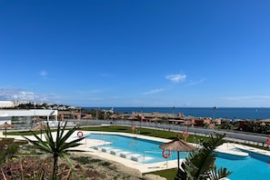 A swimming pool with a view of the ocean, surrounded by a fence and palm trees.