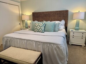 A neatly made bed with striped bedding, a bench, and multiple pillows in a bedroom with a patterned headboard.