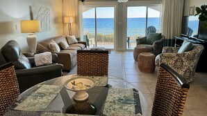 Een ruime woonkamer met uitzicht op de oceaan, ingericht met leren banken, een salontafel en een televisie.
