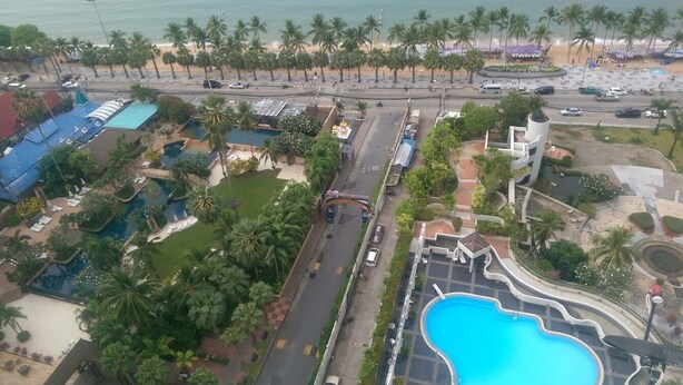 Vista aérea de un resort con piscina, palmeras y una playa.