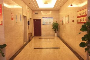 A hallway with a marble floor, a wooden door, and a potted plant. - Ruipo Hotel (Xiantao)