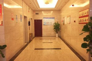 Un pasillo con piso de mármol, una puerta de madera y una planta en maceta.