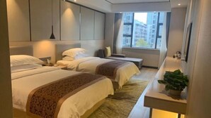 A hotel room with two beds, a bedside table, a nightstand, a large window with a view, and a potted plant. - Ruipo Hotel (Xiantao)