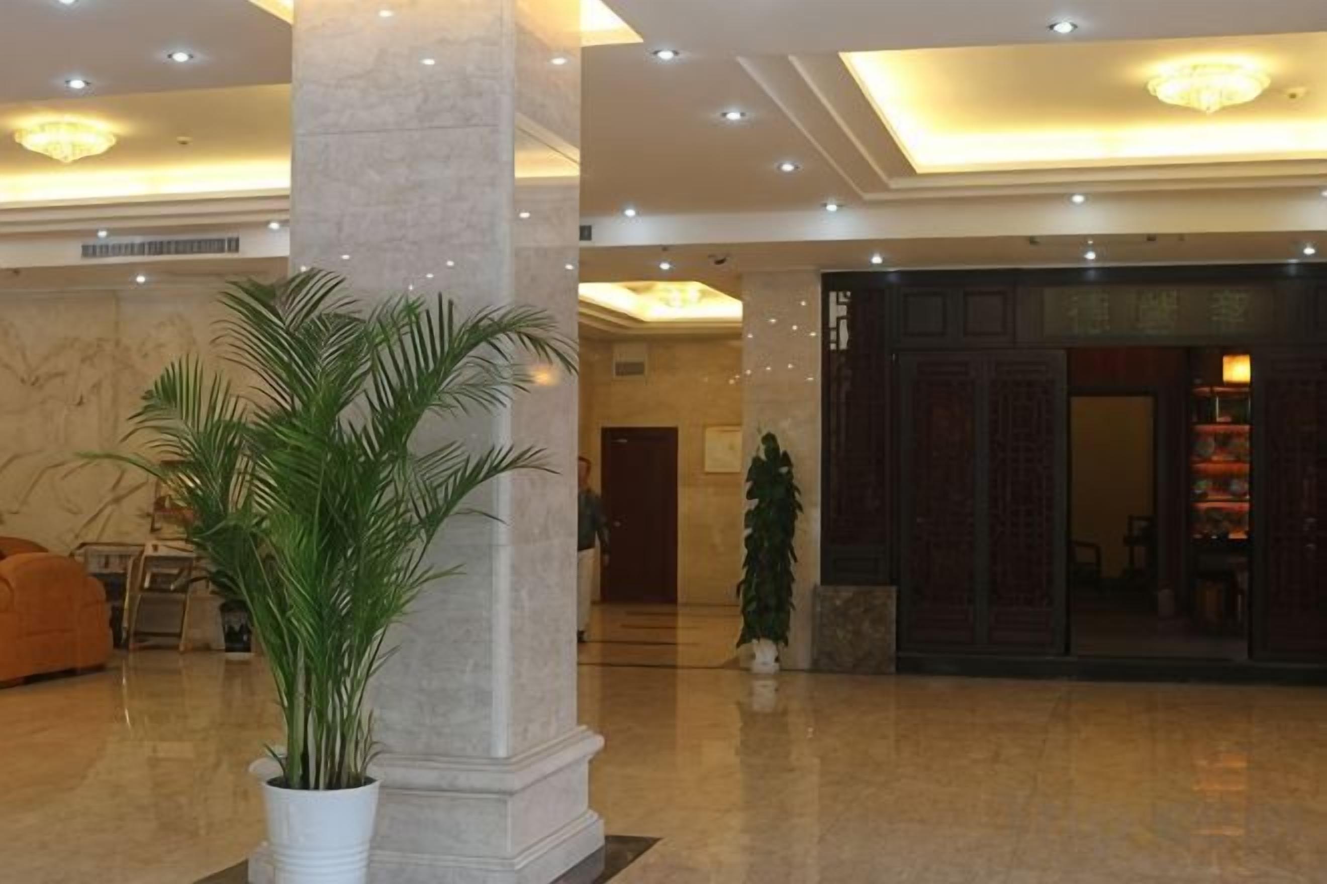 Vestíbulo con columnas de mármol, una mesa de recepción y una planta grande en maceta.